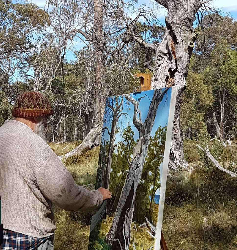 Image shows Russell McKane painting at his easel in the forest for his Artist Profile with Art Trails Tasmania story