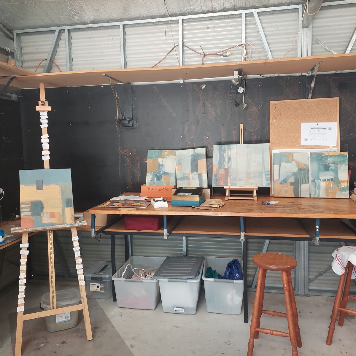 Image shows Bruny Island artist Sarah L Stewart studio space with an easel, bench, chair and four paintings in progress in her Artist Profile Story for Art Trails Tasmania