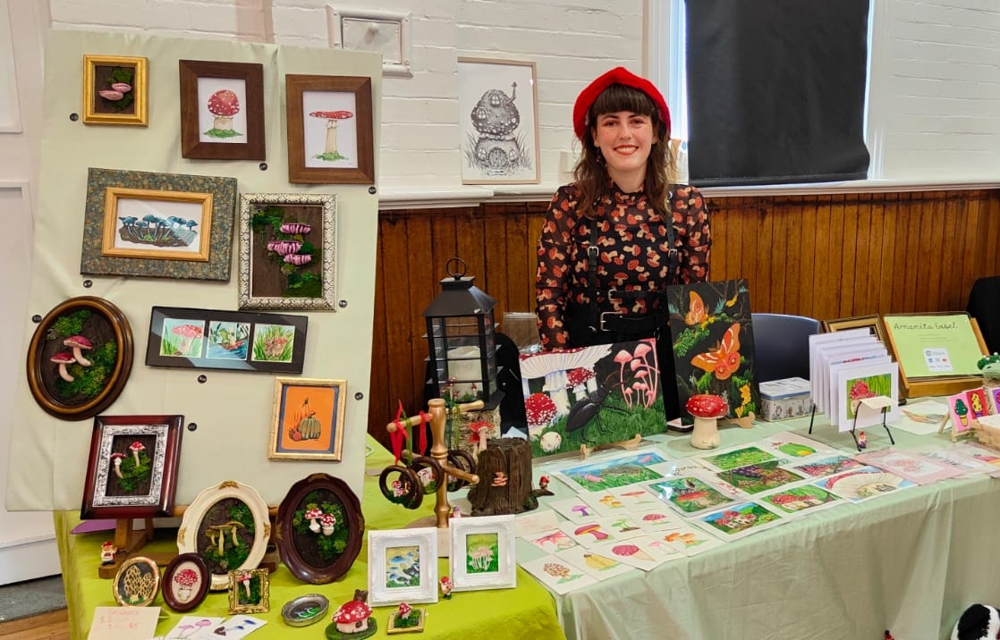 Image shows a woman at her beautiful market stall for the Artist Profile Crafting Magical Worlds and Nature's Wonders with Laurinda Brooker Art Trails Tasmania